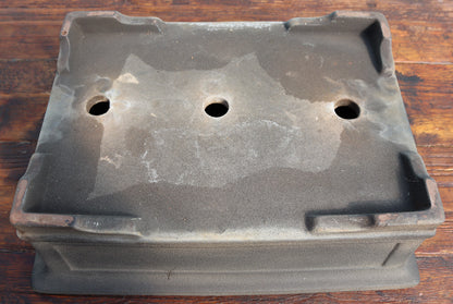 A rectangular dark gray cast iron or ceramic planter with three circular drainage holes on top, resting on a wooden surface.