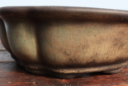 Close-up of a ceramic bonsai pot with a textured, metallic bronze-brown glaze resting on a rustic wooden surface.