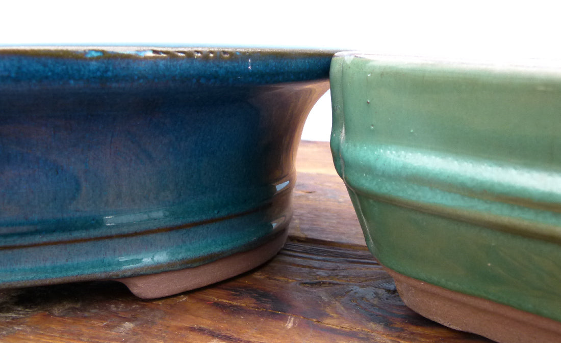 Two ceramic pots, one blue and one green, on a wooden surface.